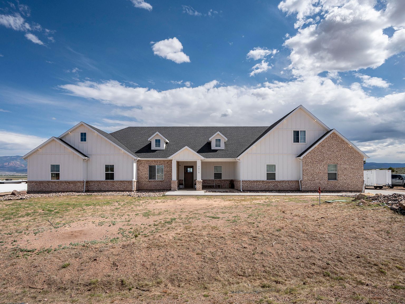 Front elevation of 7015 W 1300 N, white board-and-batten gables flanked by warm brick wings, under a wide Cedar City sky